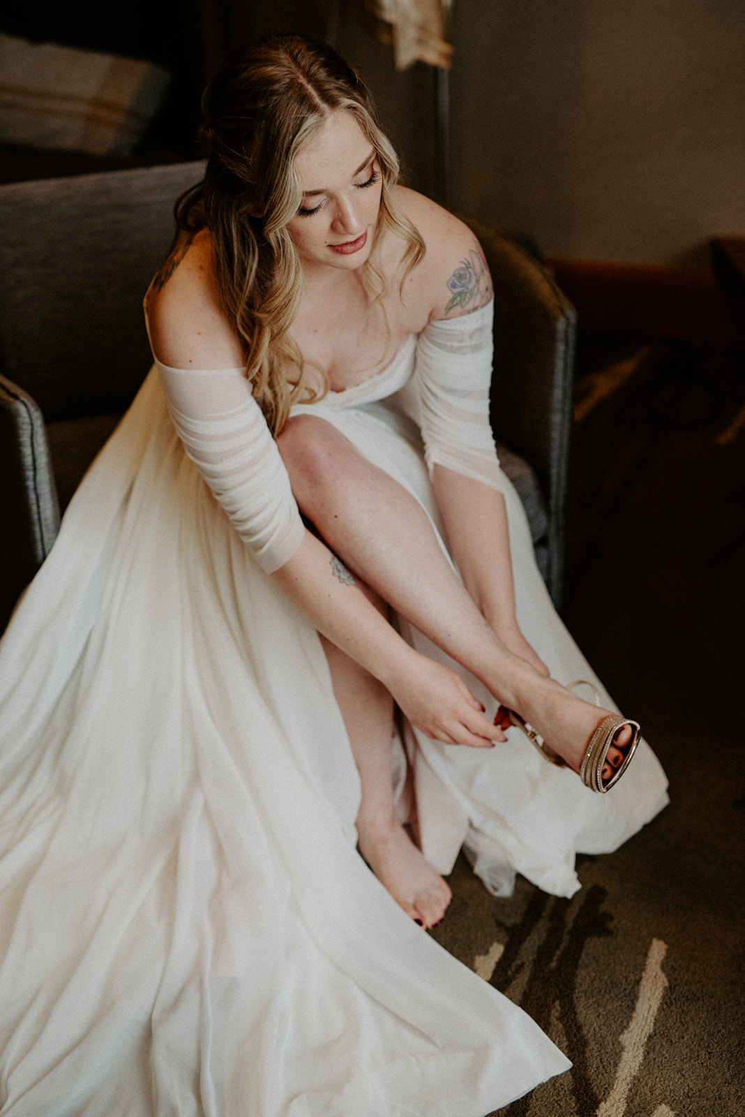 Bride carefully putting on her wedding shoes while seated in her gown before the ceremony