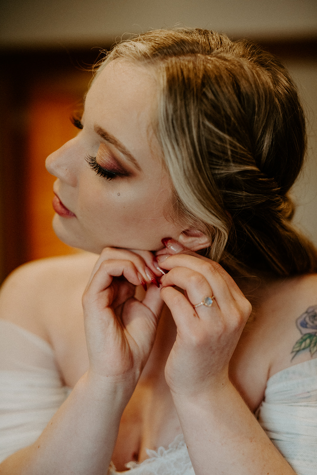 Close portrait of a bride putting on an earring with her eyes closed, captured during getting-ready coverage