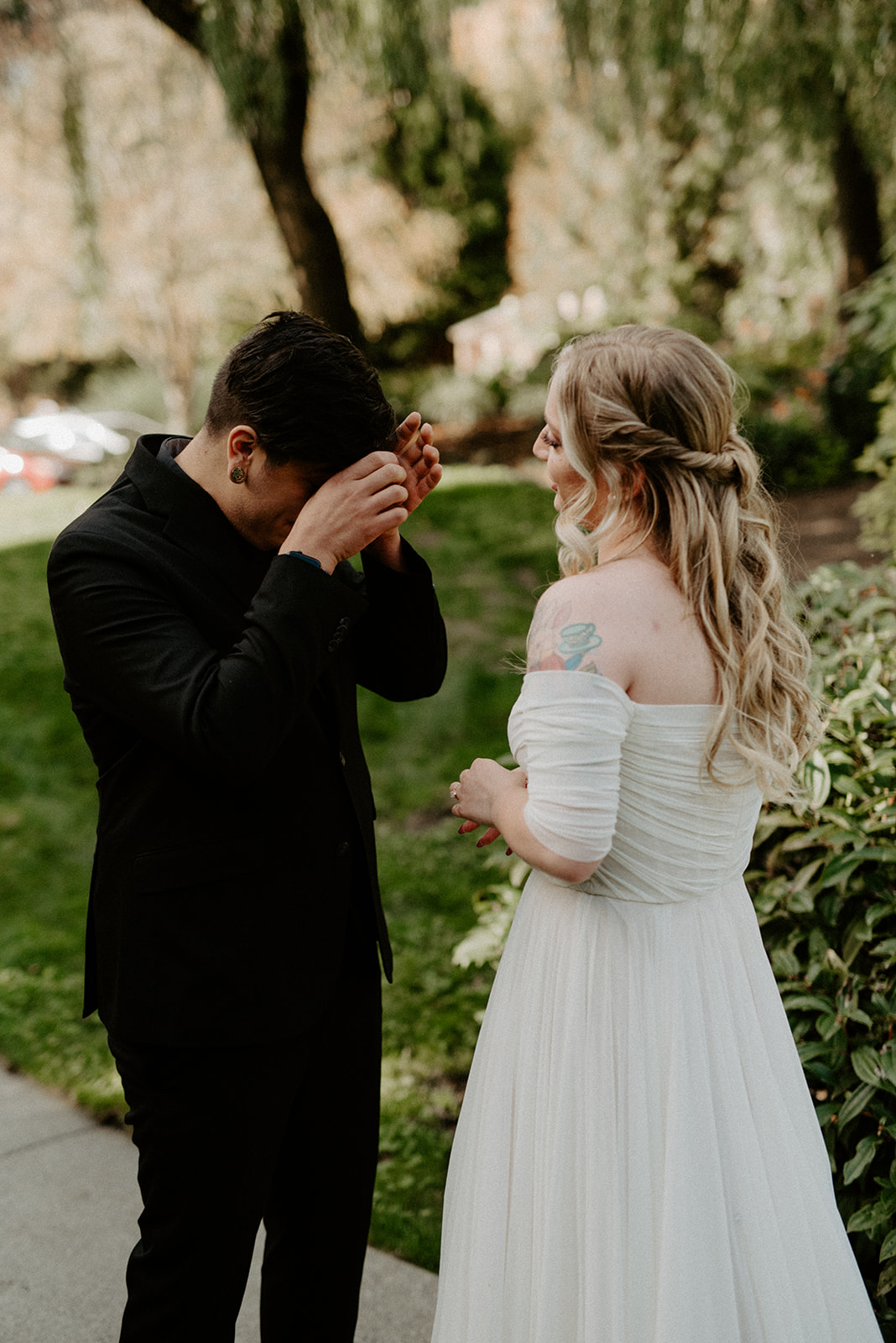 Groom wiping tears during an emotional first look, bride facing away in her off-shoulder wedding gown