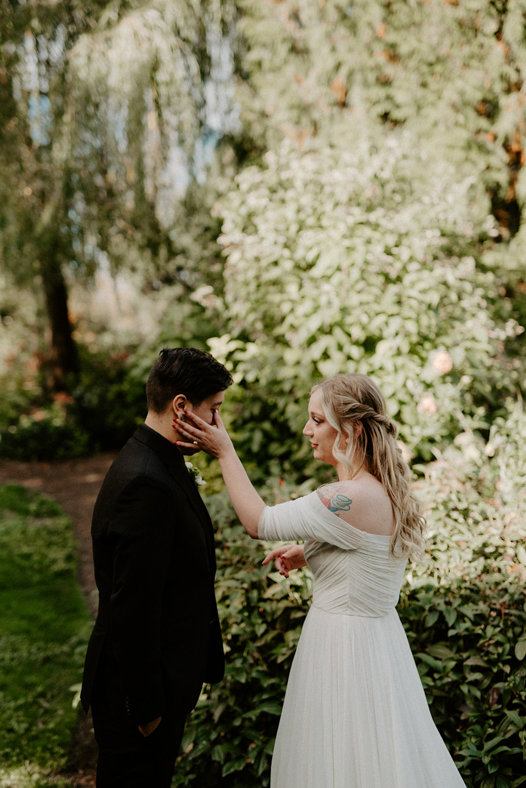 Bride gently touching the groom's face while wiping tears during their first look in the garden