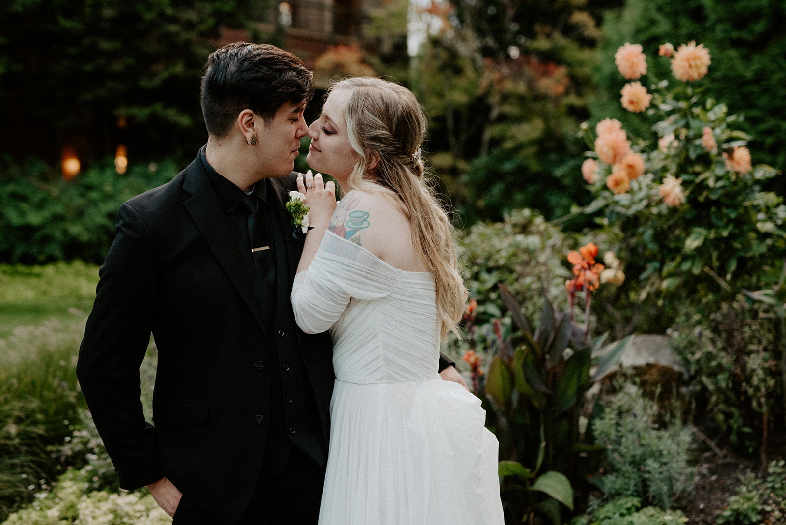 Couple sharing a quiet moment in the dahlia garden at Willows Lodge, he leans in as she holds a flower