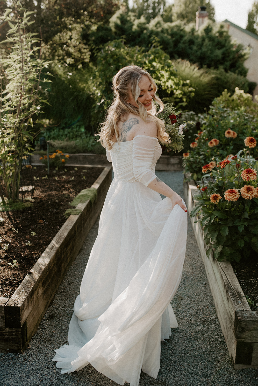 Bride standing alone on a garden path at Willows Lodge, her flowing white gown catching the light among dahlias