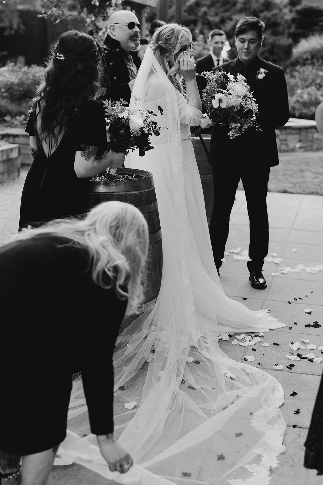 Black and white image of the bride arriving at the altar, her long veil trailing behind her as the groom waits ahead