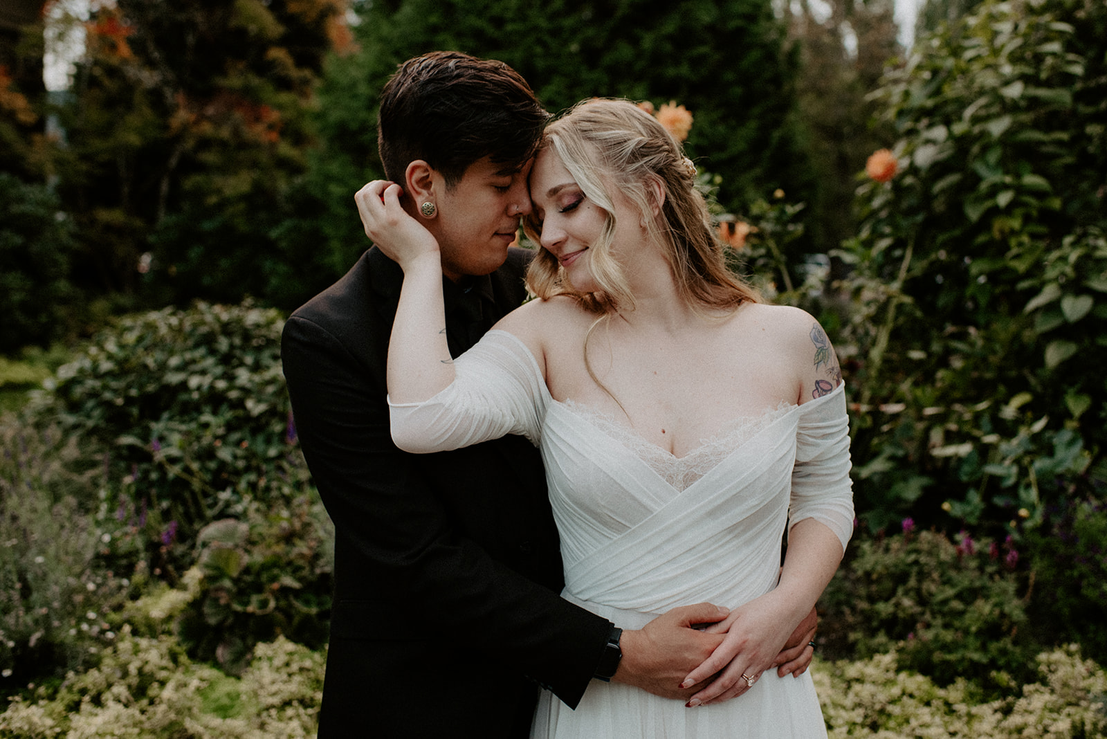 Close portrait of a bride and groom with foreheads touching, surrounded by soft garden greenery