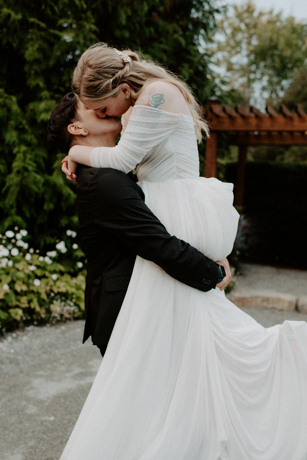Groom dramatically lifting his bride in the garden, her dress sweeping out, surrounded by blooms
