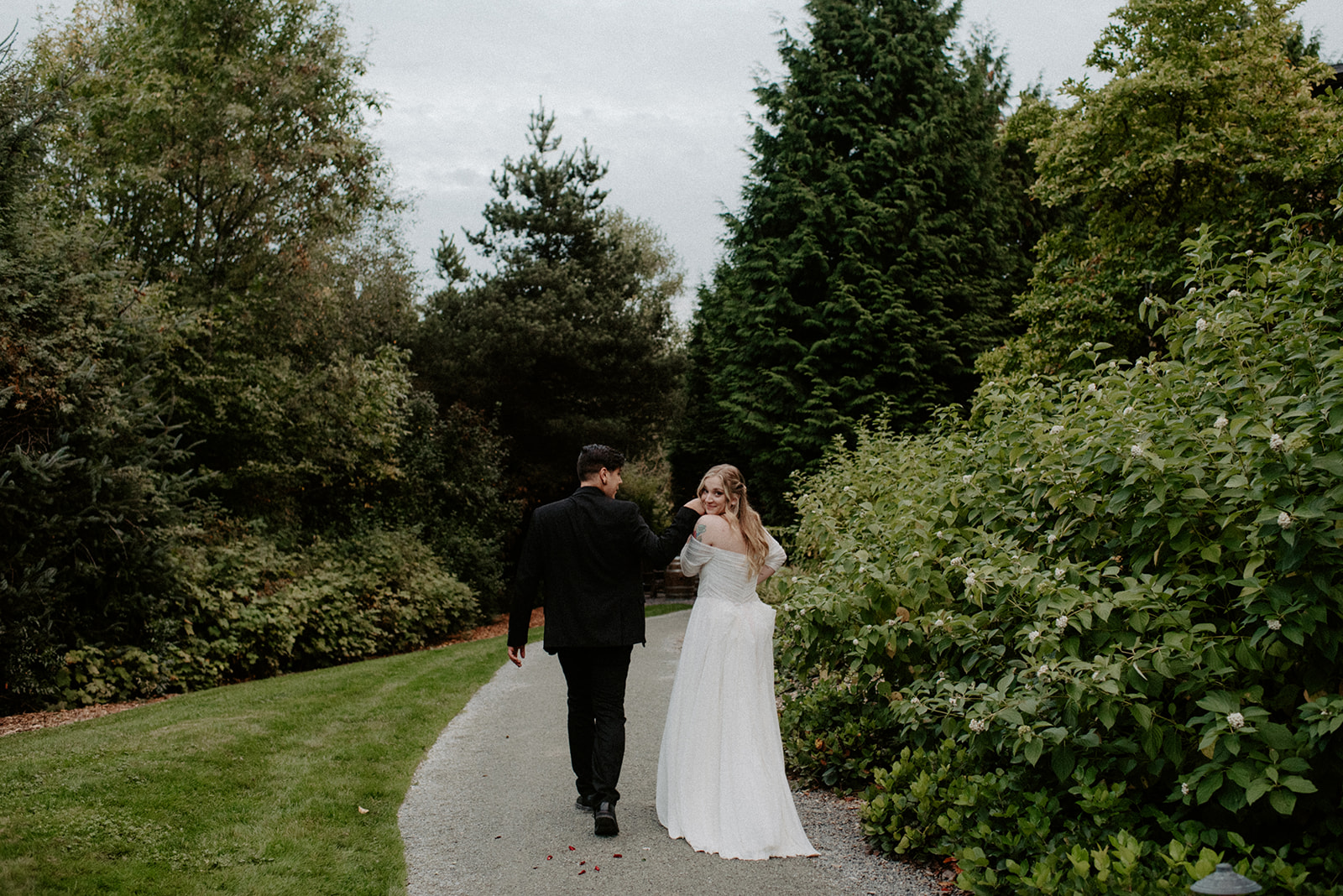 Couple walking hand in hand down a lush garden path at Willows Lodge, bride looking back over her shoulder