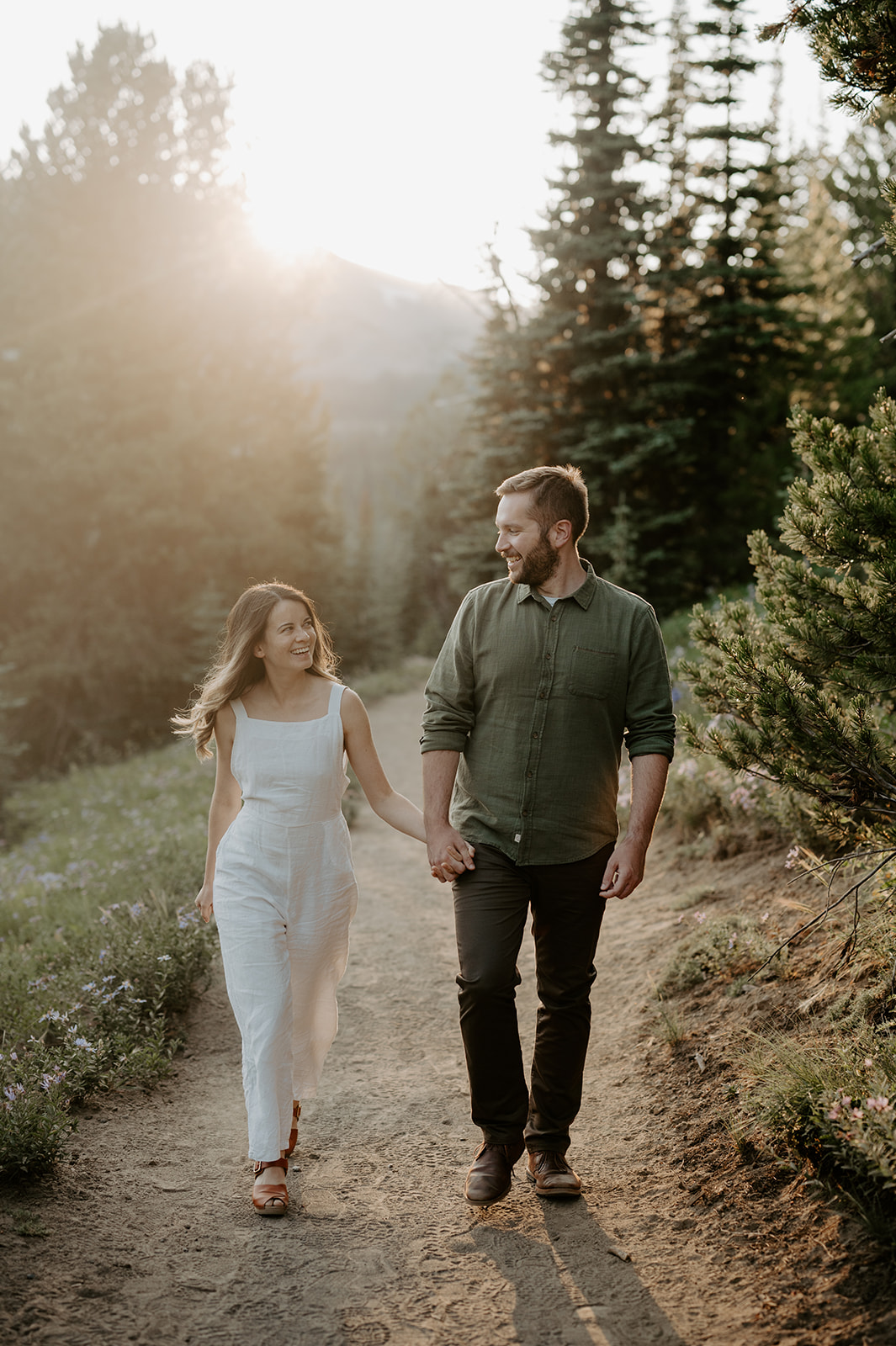 A couple walking hand in hand on a forest path, with the sun setting behind them.