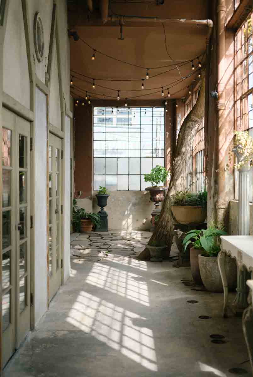 An enchanting indoor courtyard at The Ruins in Seattle, featuring potted plants, string lights, and large windows casting beautiful natural light.