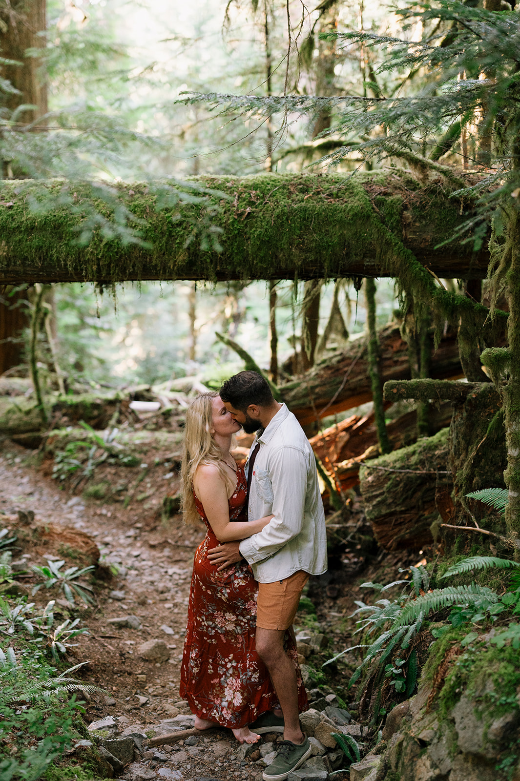 R and M kissing under a moss-covered log in the forest.