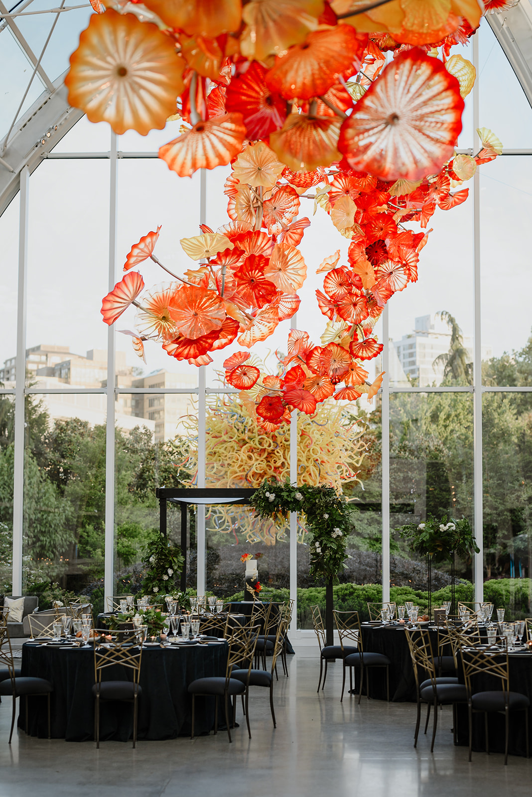 Round tables set with black tablecloths under vibrant glass flower installation at Chihuly Garden.