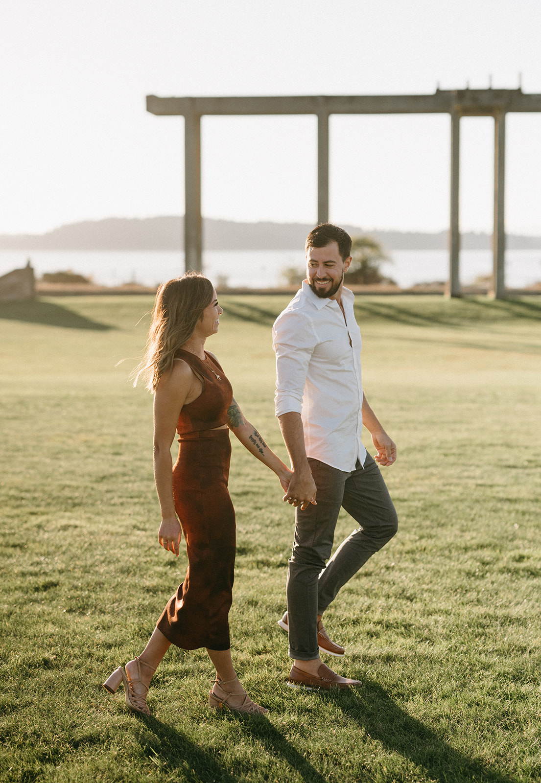 A couple holding hands and walking on the grass at Chambers Bay during their engagement session.