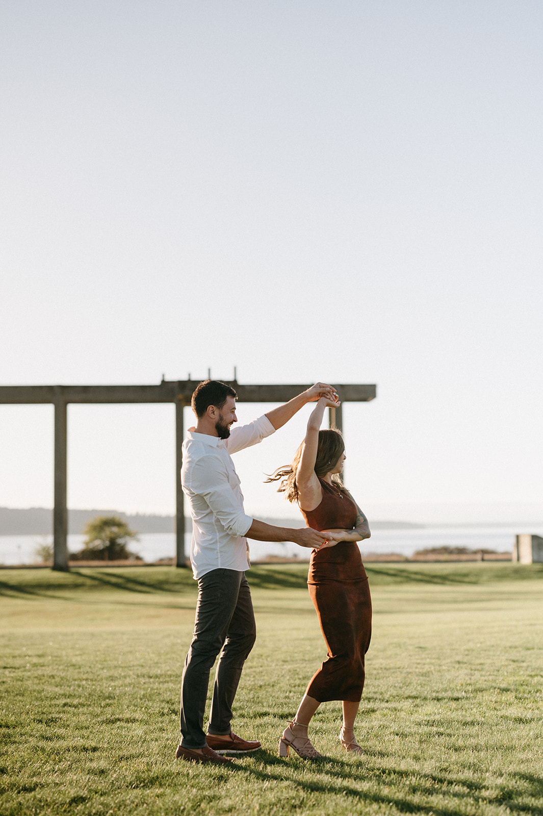 A couple dancing together on the grass at Chambers Bay with the Puget Sound in the background.