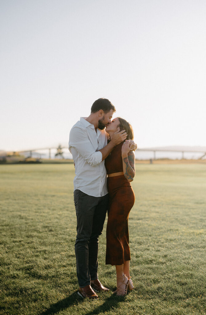 Couple sharing a kiss in an open field during sunset.