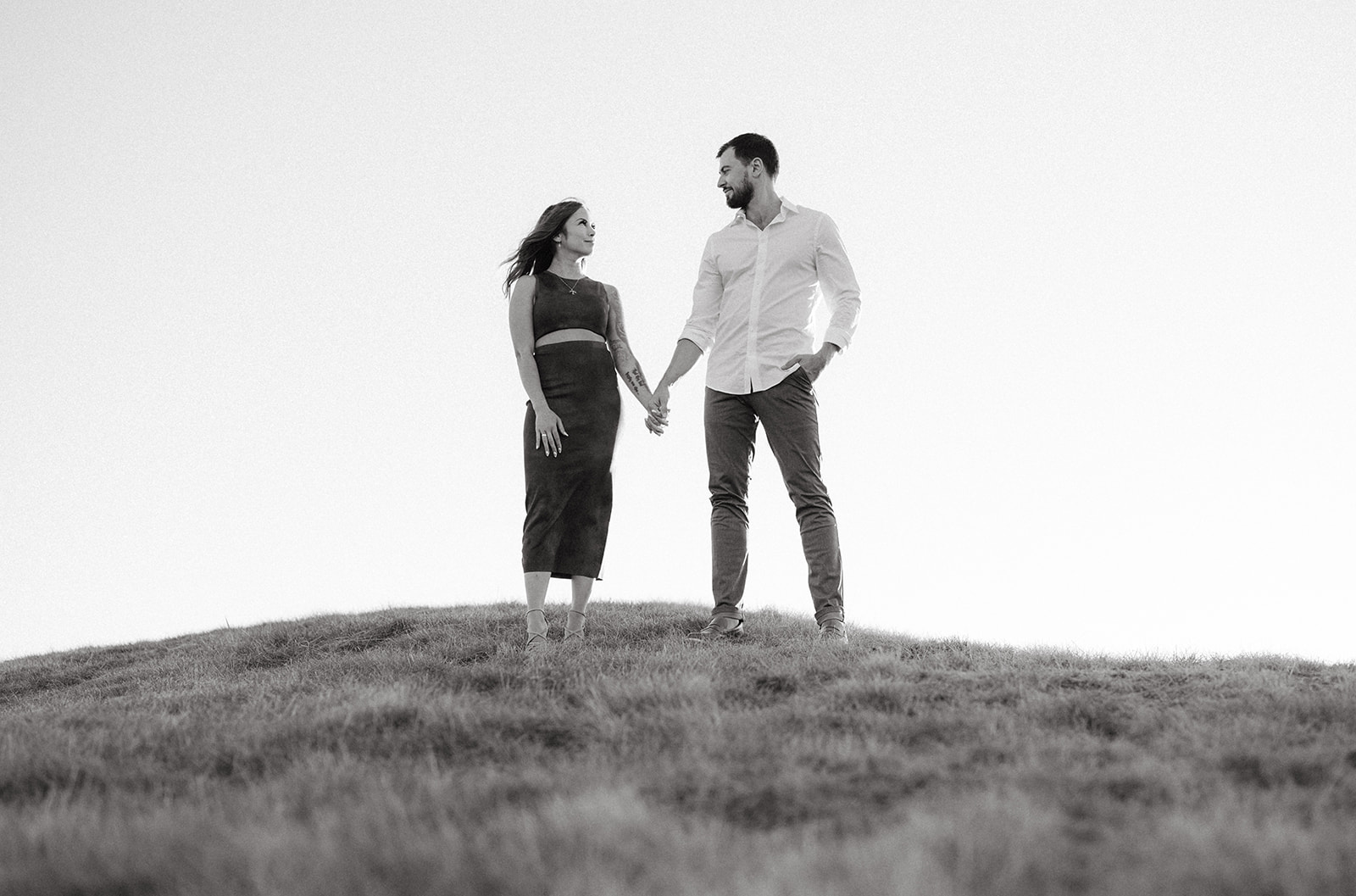 A couple holding hands on a grassy hill with a clear sky.