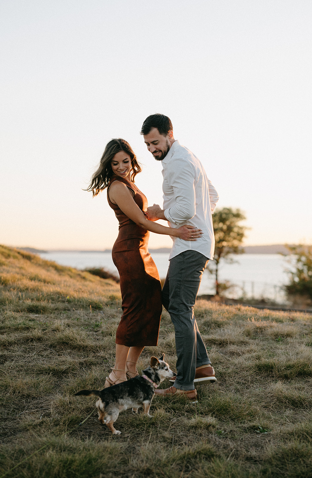 A couple dancing on a grassy hill with their dog.