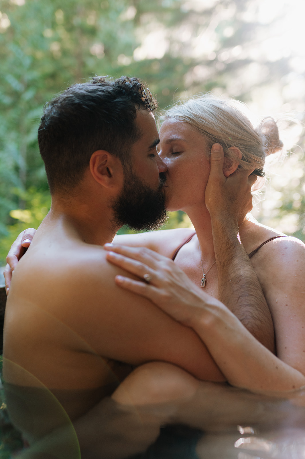 R and M sharing a kiss in a hot spring, surrounded by greenery.