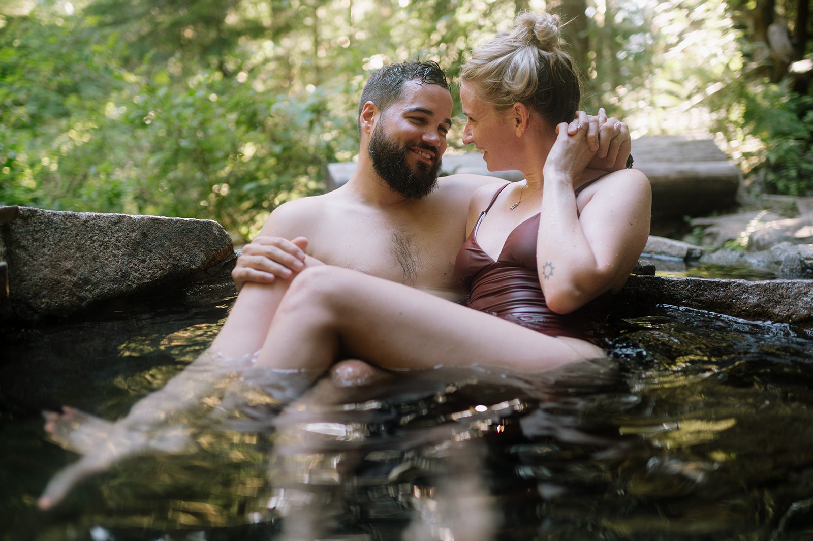 R and M smiling at each other while relaxing in a hot spring.