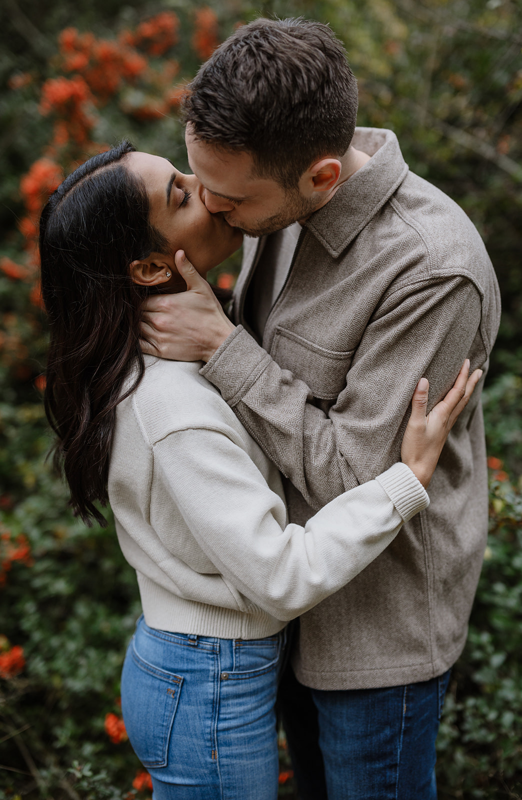 Couple shares a kiss surrounded by red holly bushes at Discovery Park.