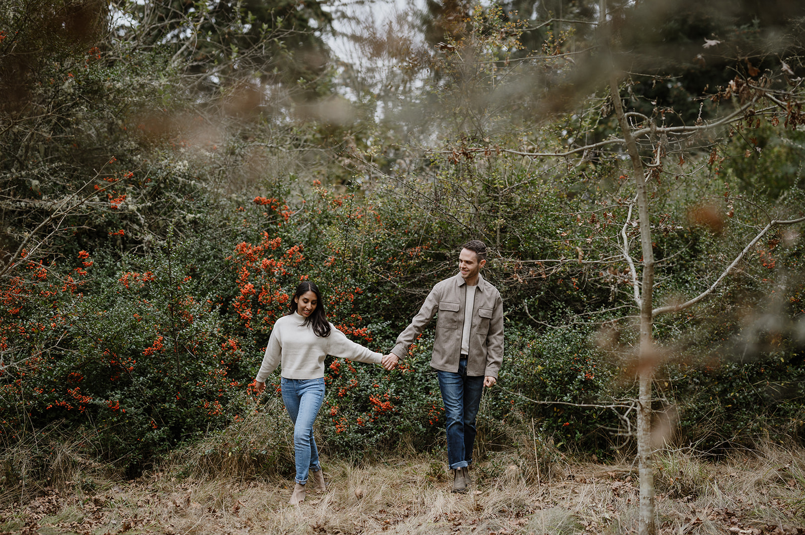 Couple walking through red holly bushes and fall foliage at Discovery Park.