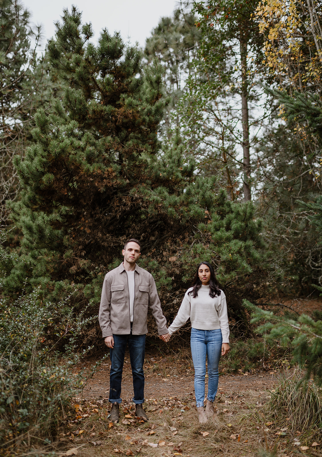 Couple standing together holding hands surrounded by tall trees in Discovery Park.