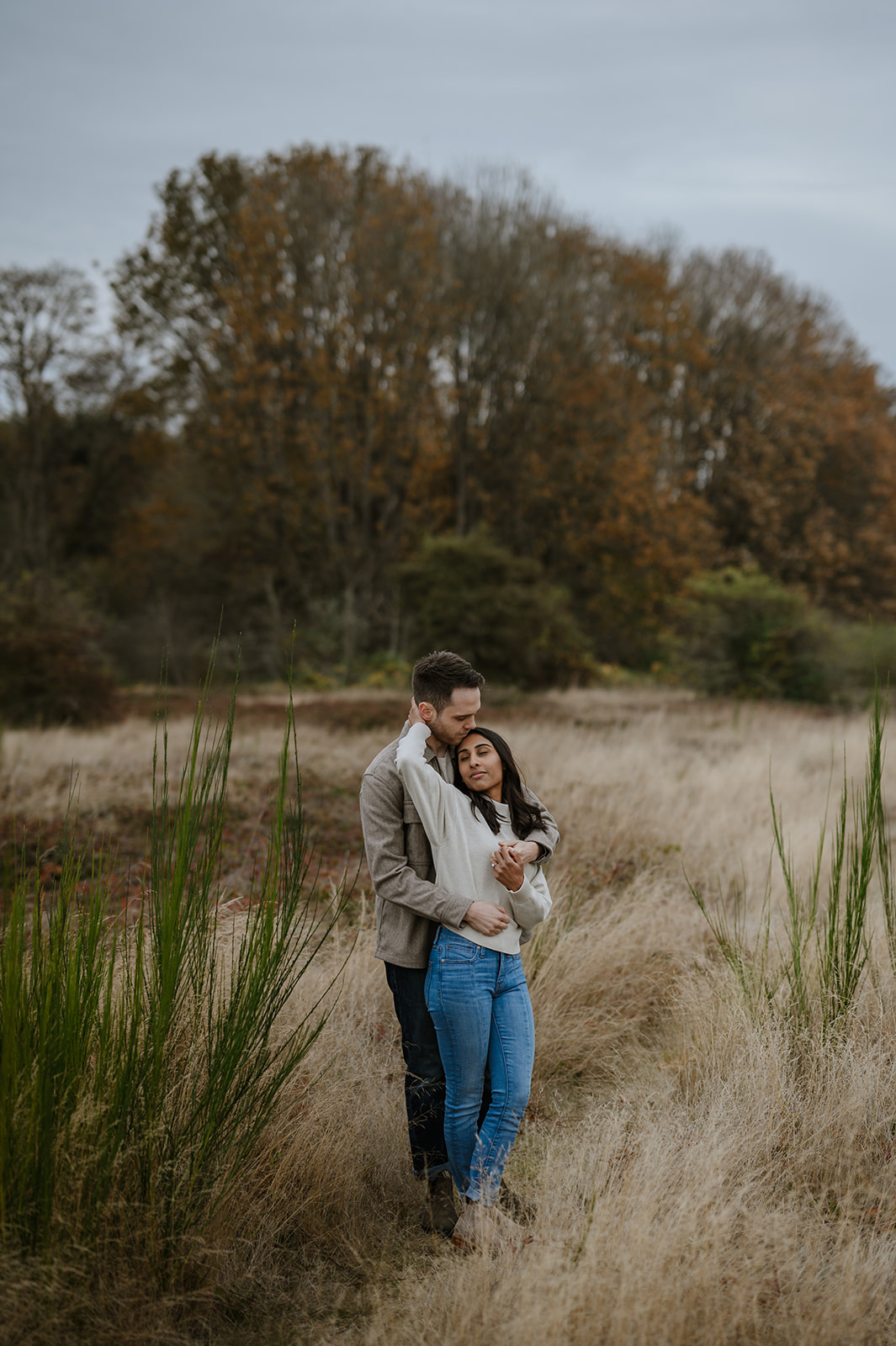 Couple embraces in a grassy field at Discovery Park during the fall season.