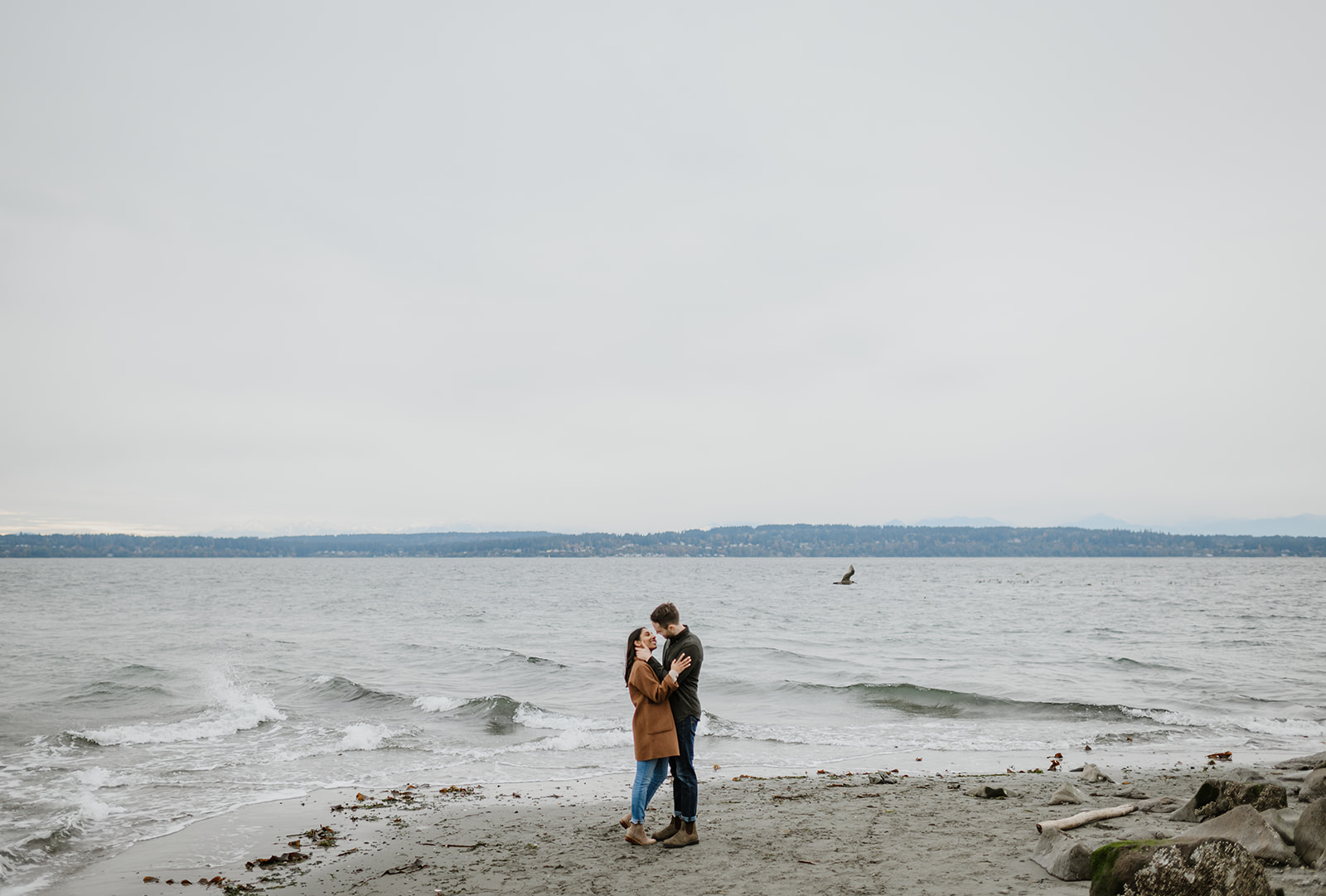 Couple embracing on the beach while looking out at the ocean waves.