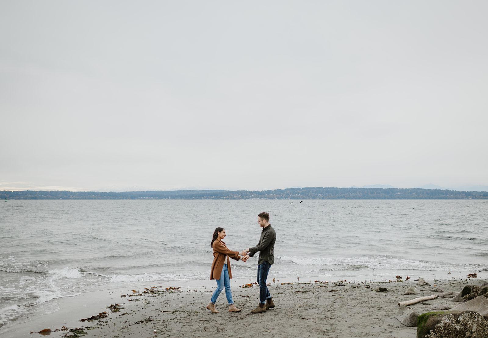 Couple holding hands while dancing on a beach with the ocean in the background.