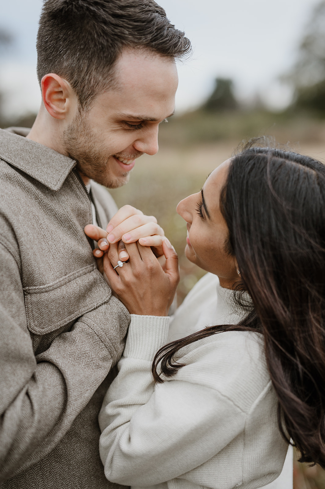 Couple smiling at each other and holding hands during their engagement session at Discovery Park in fall.