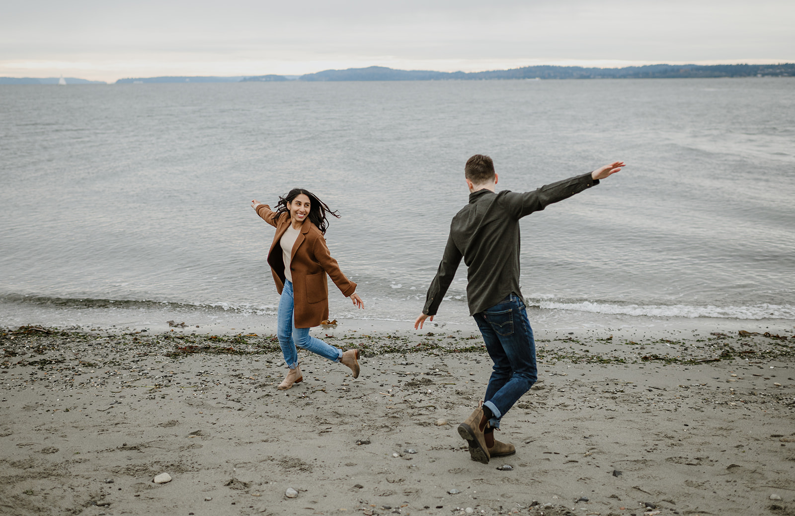 Couple running and playing along the beach, full of laughter and joy.