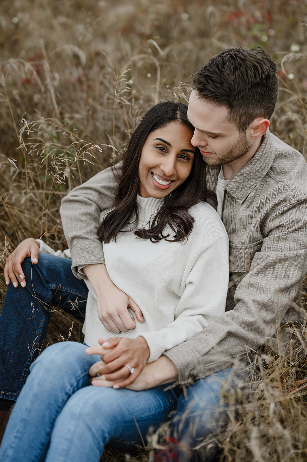 Couple seated in a field at Discovery Park, with the woman smiling and leaning into her partner's embrace.