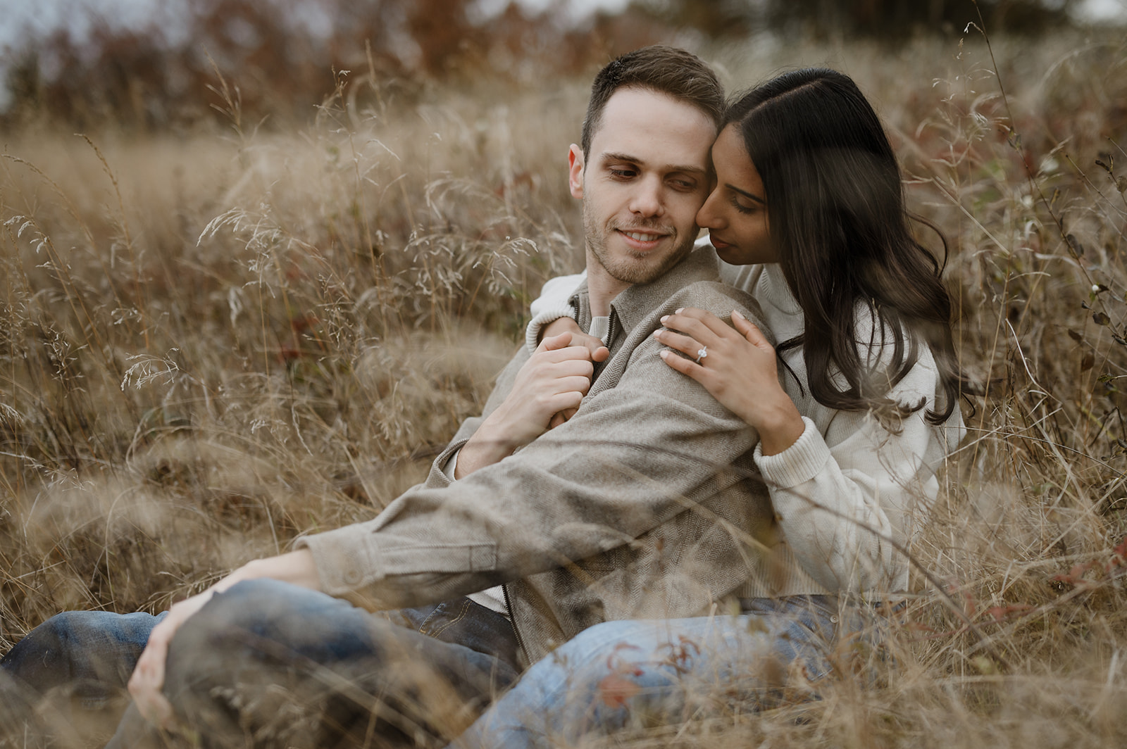 Couple sharing an affectionate moment, cuddling in a field surrounded by autumn grasses.