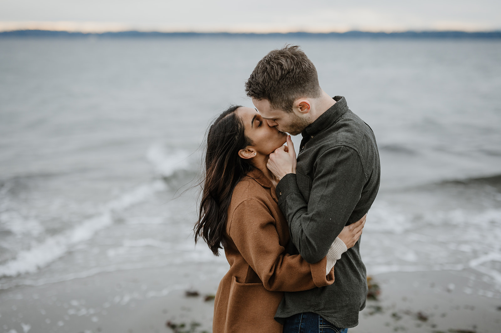 Couple kissing passionately in front of the ocean waves during their engagement session.