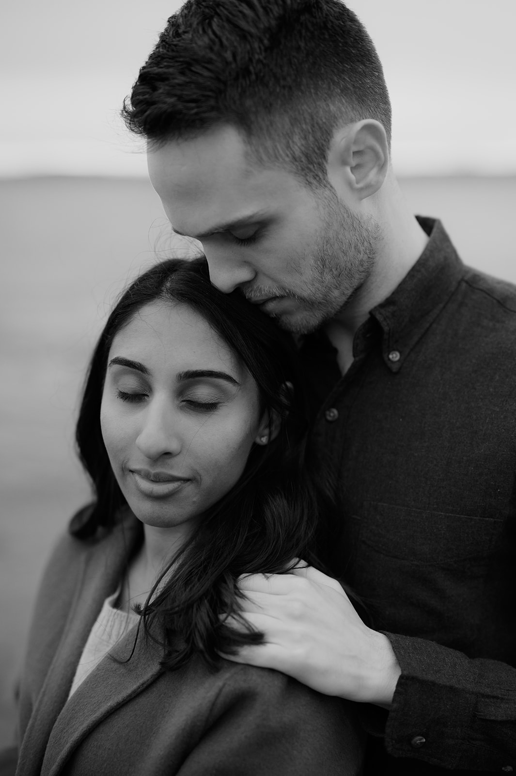 Couple standing close with eyes closed, resting their heads together on the beach.