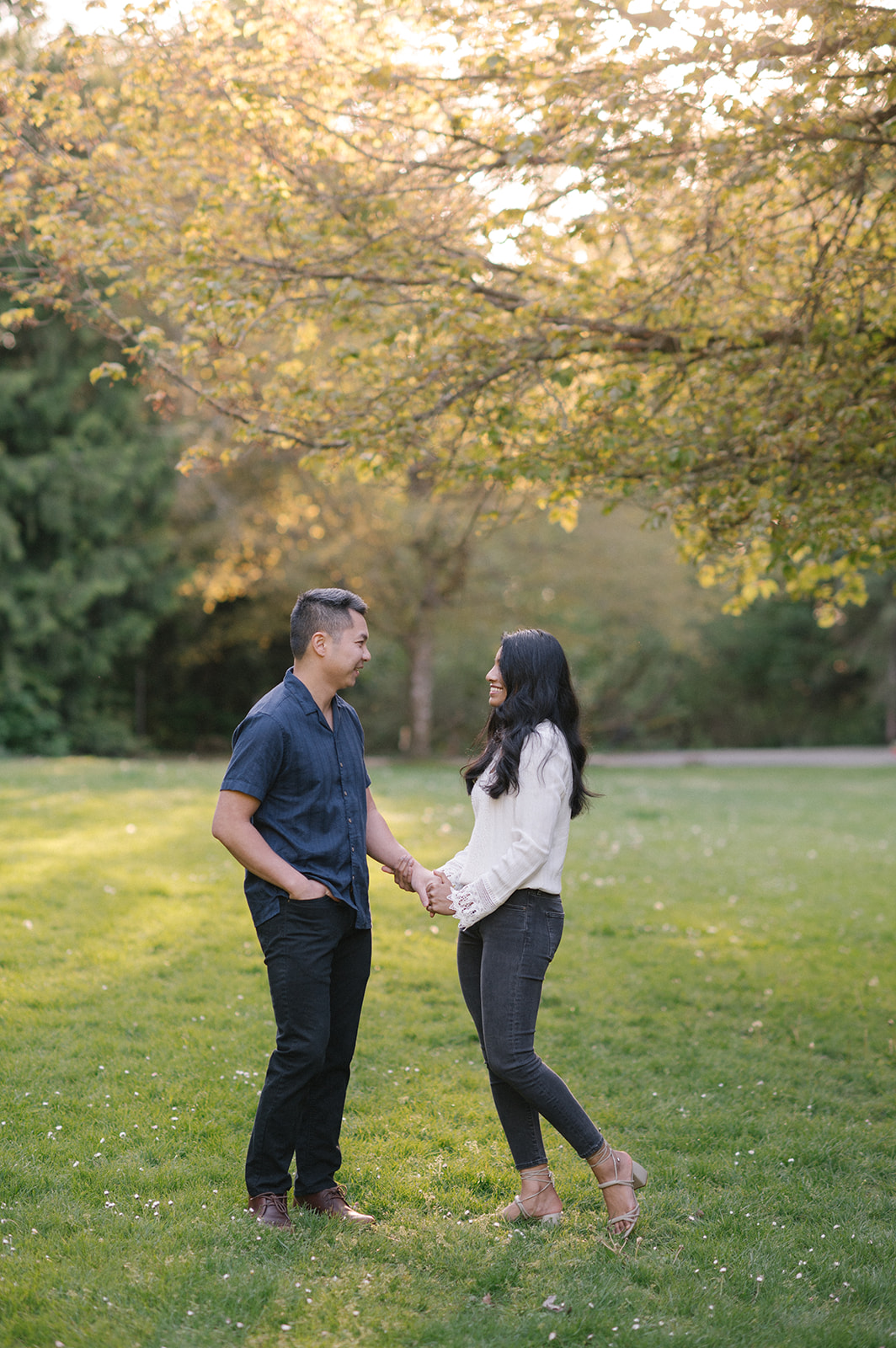 A couple holding hands and smiling at each other in the park.