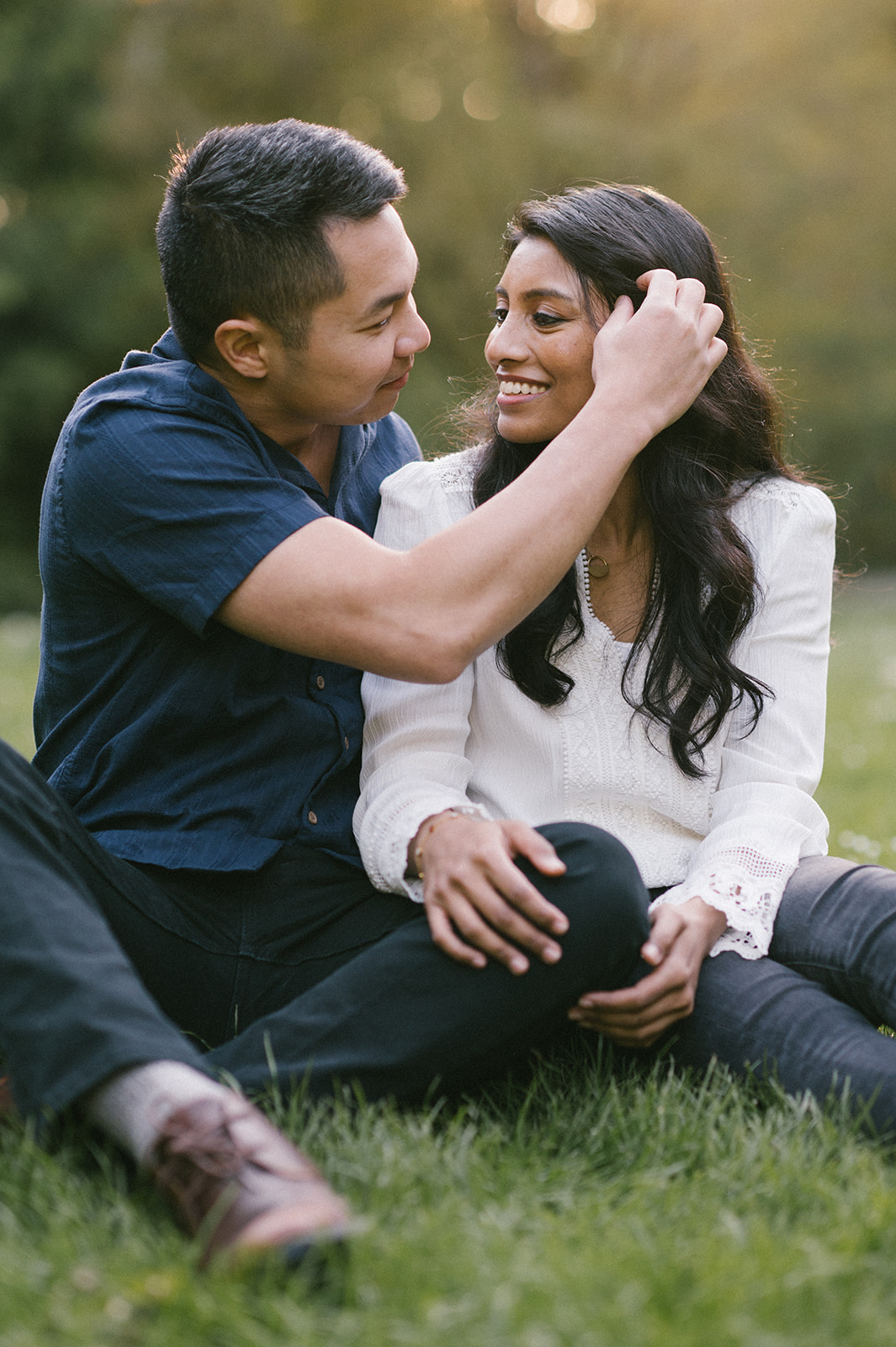 A couple sitting on the grass, the man brushing the woman's hair gently.