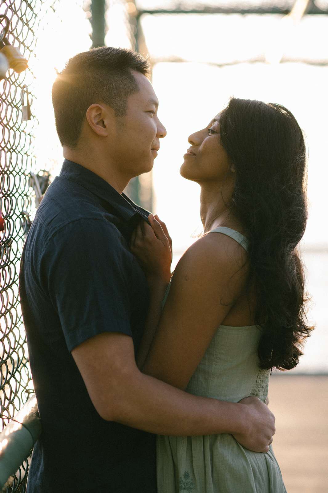 A couple gazing into each other's eyes, holding each other close on a bridge at sunset.