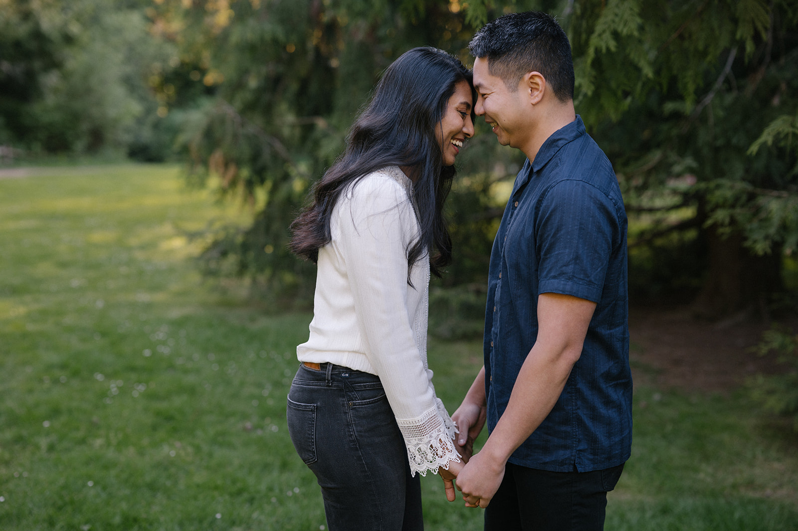 A couple sharing a tender moment, touching foreheads and holding hands in the park.