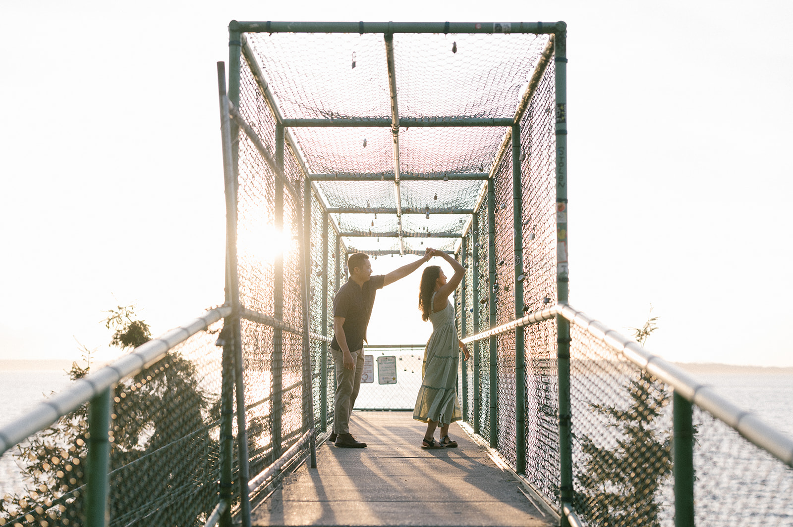 A couple dancing on a bridge at sunset, surrounded by a wire fence.