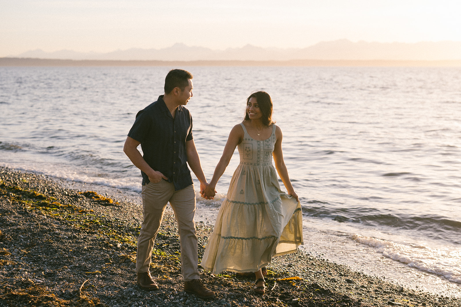 A couple enjoying a walk on the beach, smiling at each other.