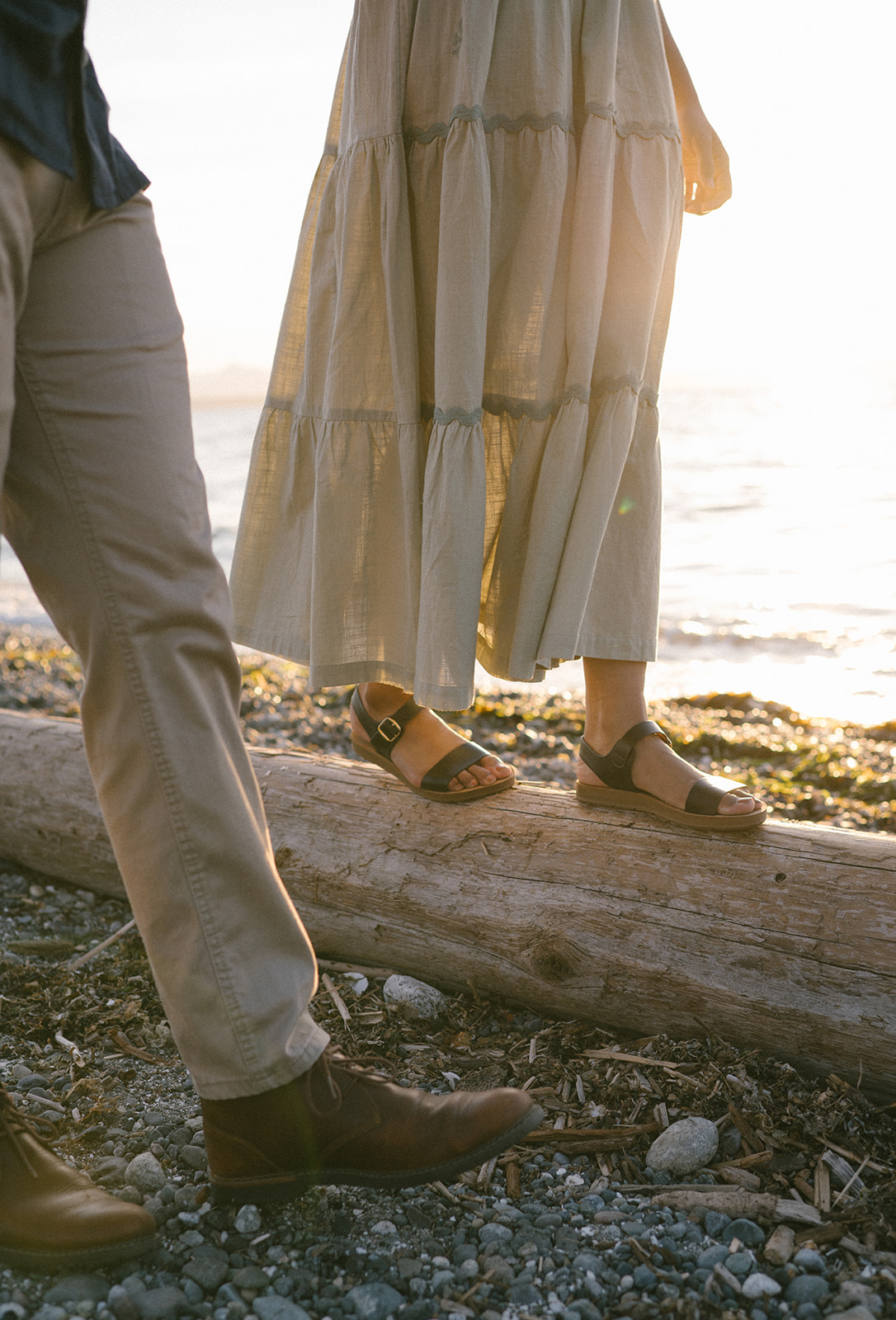 Close-up of a couple's feet as they walk on a log by the beach.