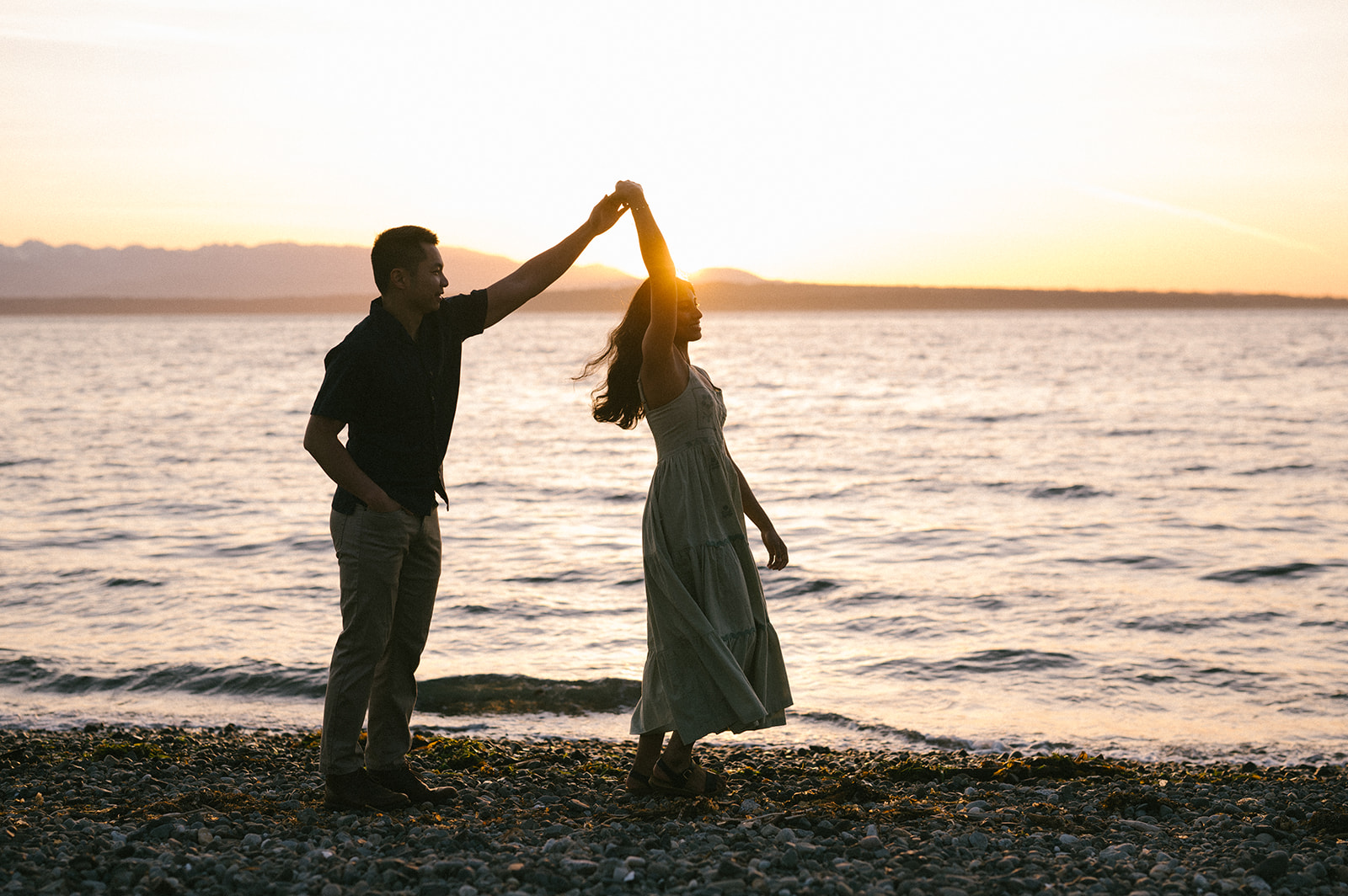 A couple dancing by the water at sunset, with the sun creating a warm glow.