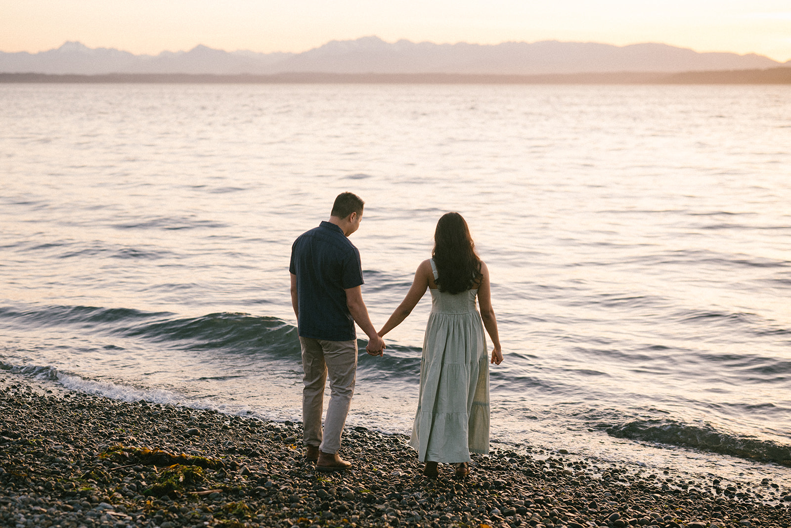 A couple holding hands with a blurred mountain view in the background at sunset.