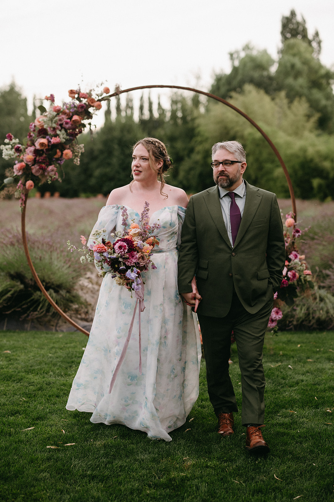 Couple walking past a circular floral arch holding hands after their ceremony.