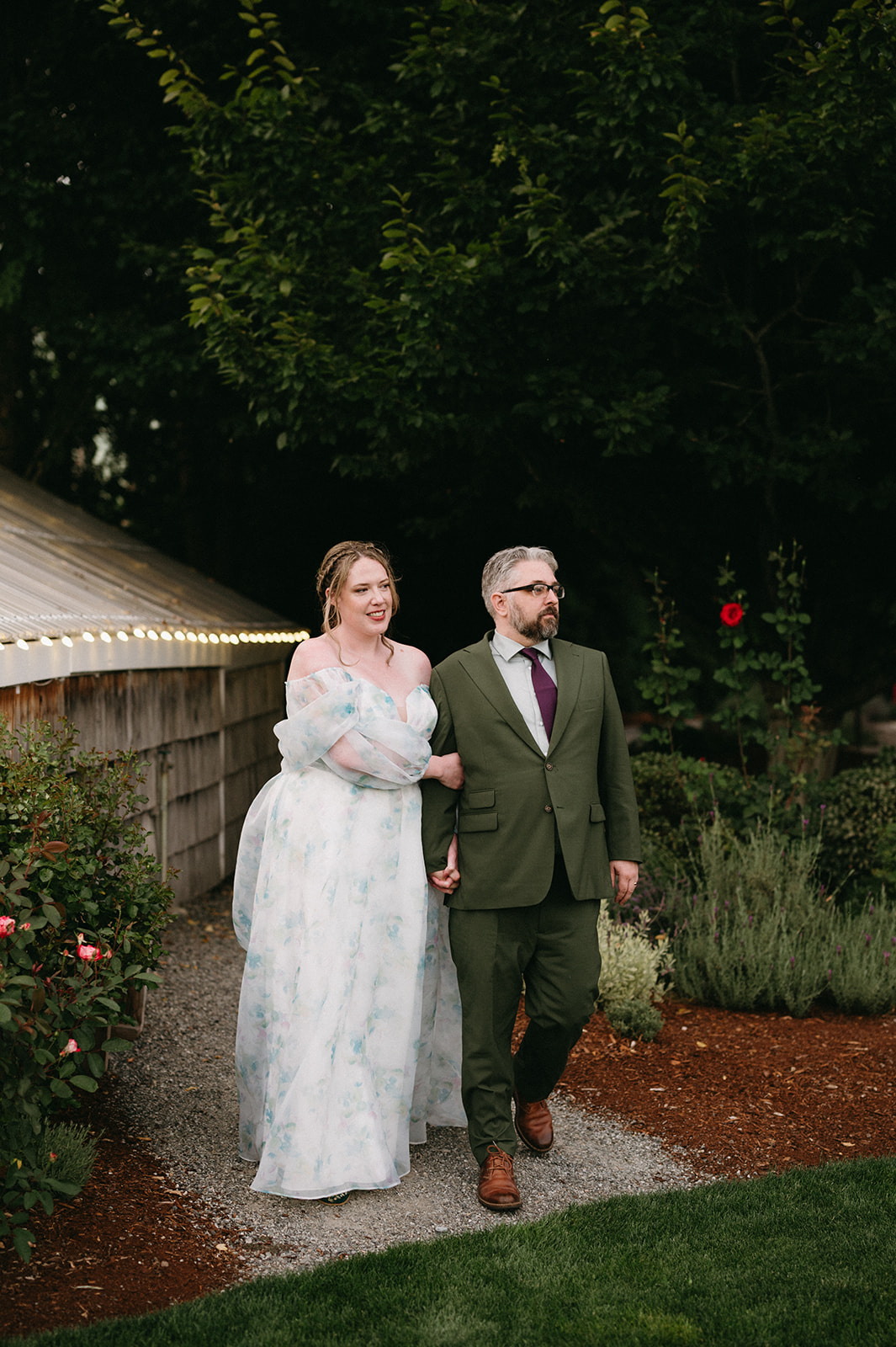 Couple walking arm in arm along a garden path beside a greenhouse at twilight