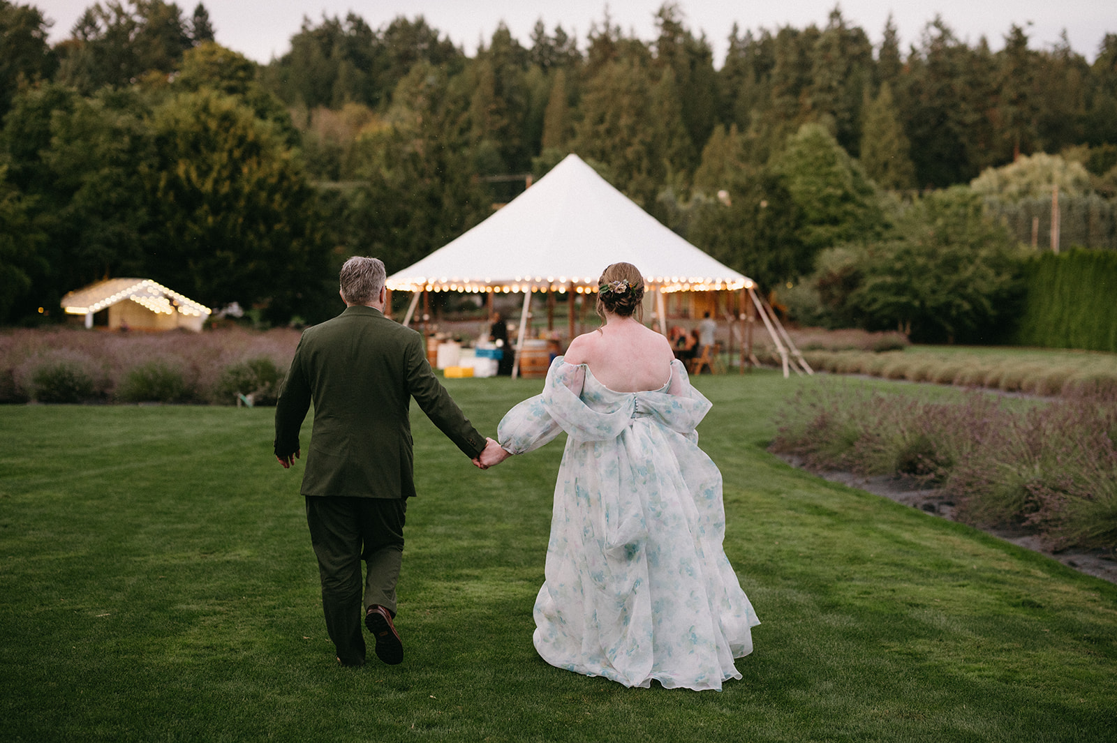 Couple walking hand in hand toward a glowing tent at dusk