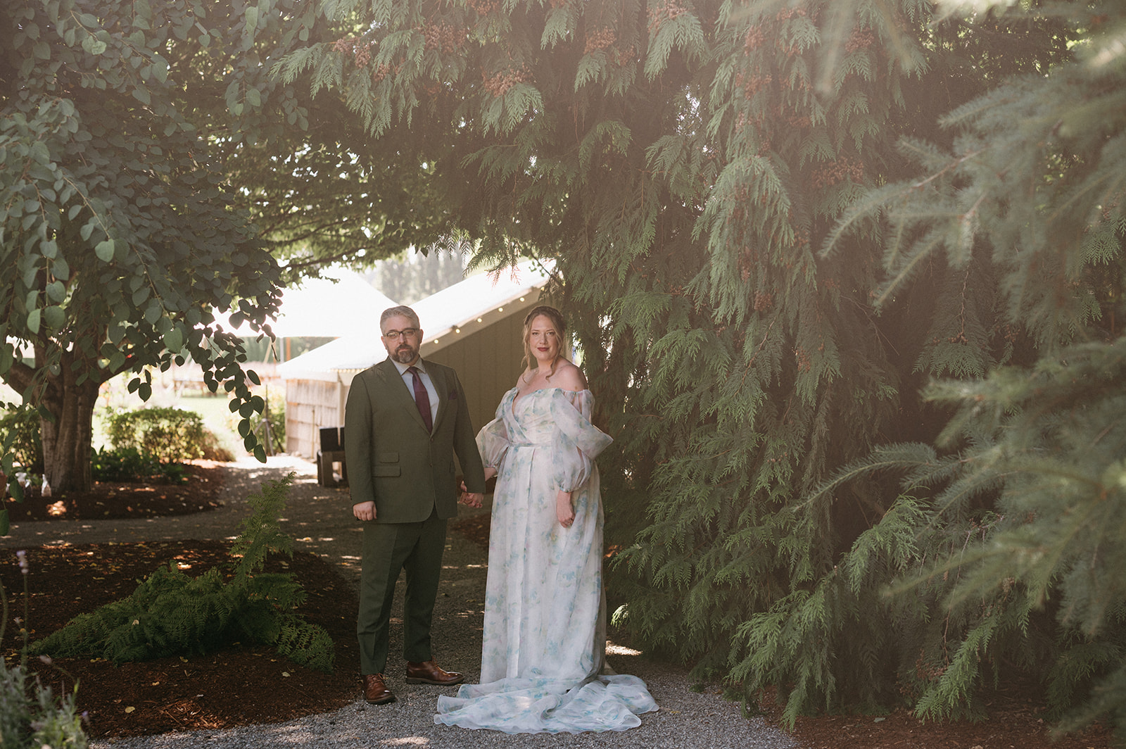 Couple walking hand in hand, exchanging smiles beneath evergreen trees
