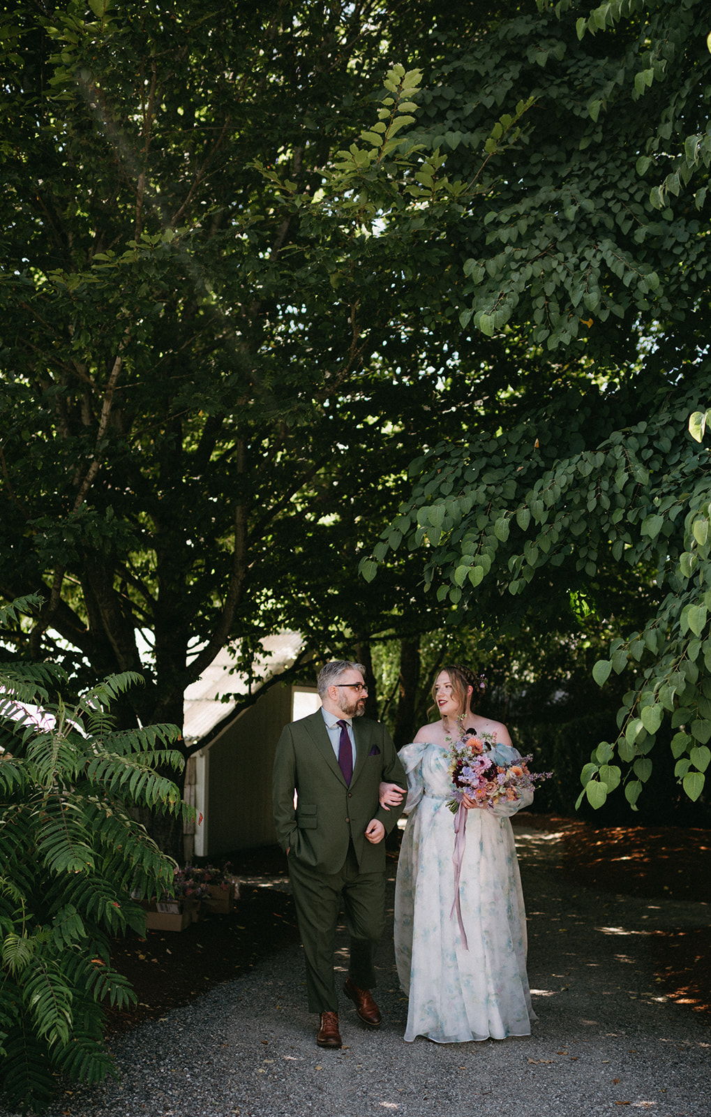 Couple walking arm in arm beneath leafy canopy, smiling at each other