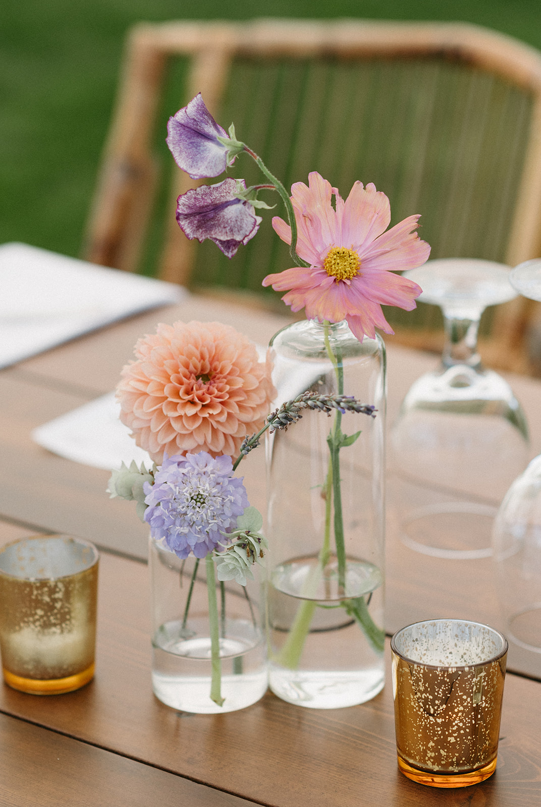 Trio of delicate flowers in clear vases on wooden table
