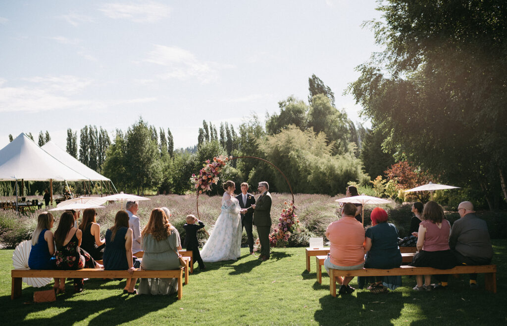 Creative wedding ceremony at a lavender farm with parasols, wooden benches, and a circular floral arch