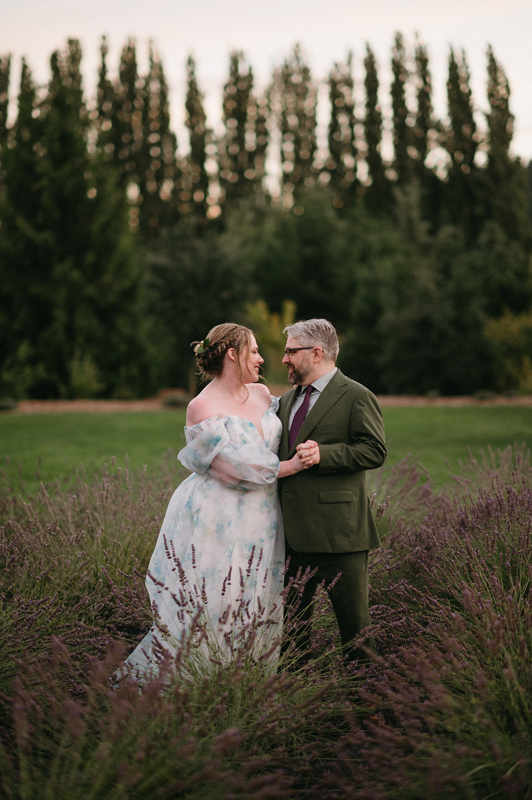 Couple standing close in a lavender field at sunset, looking at each other lovingly.